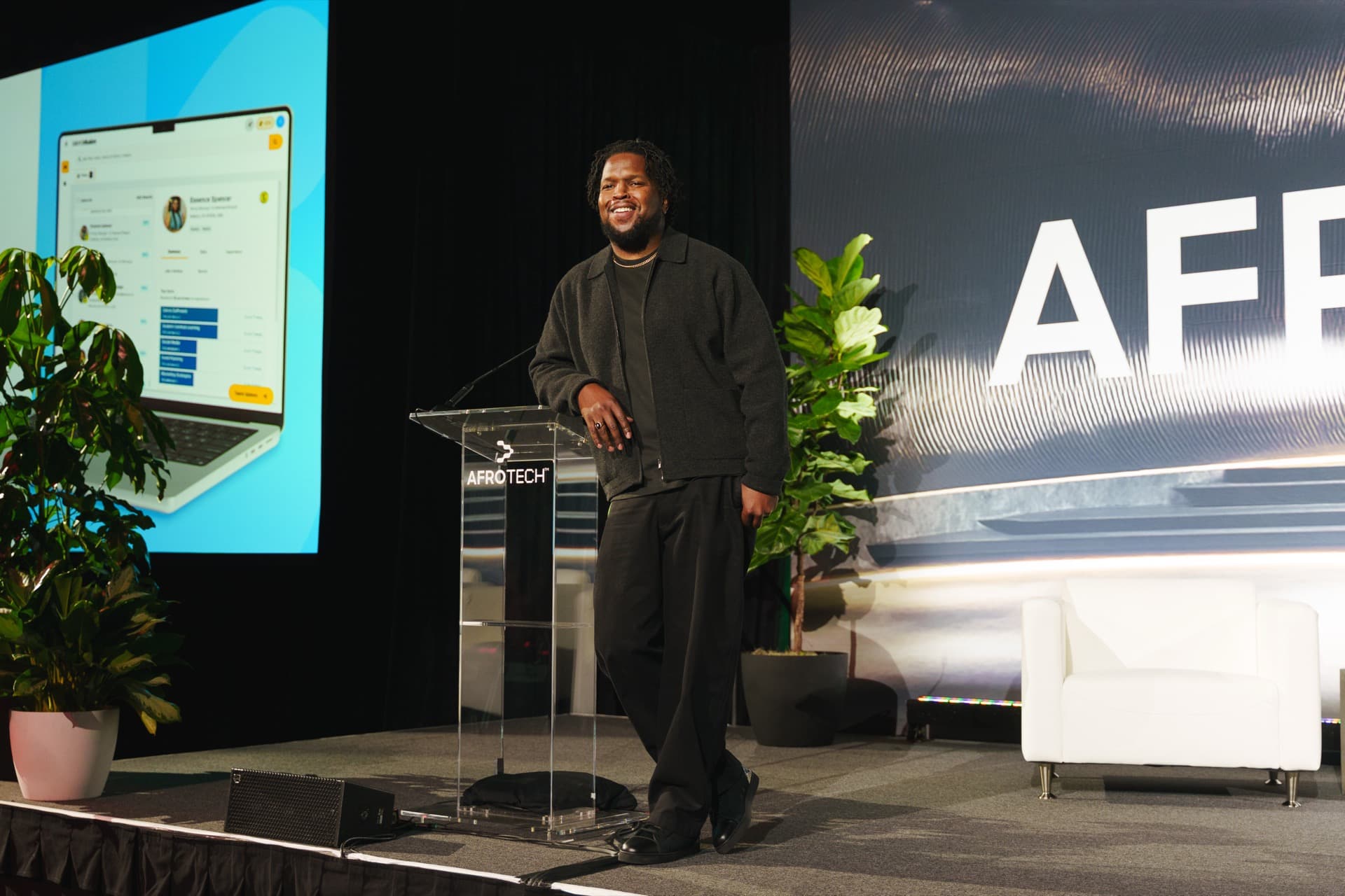 Will Lucas smiling on stage, leaning on a clear AfroTech podium.