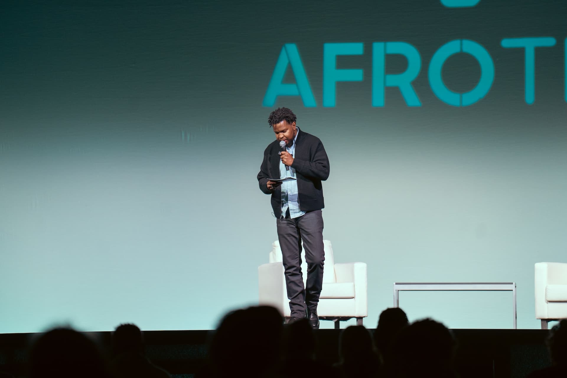 Will Lucas on stage at AfroTech with the AFROTECH wordmark behind him, reading from notes.