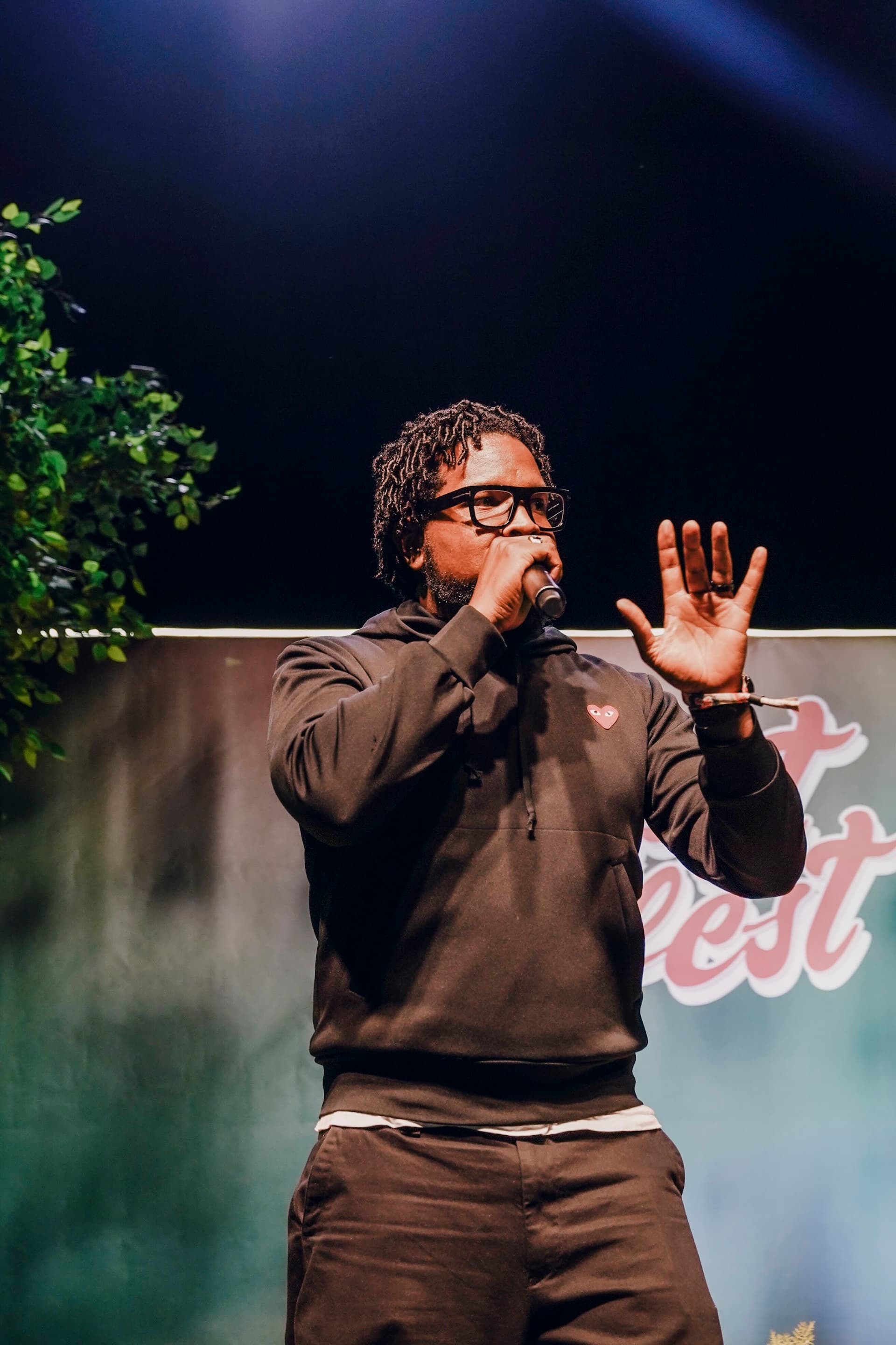 Will Lucas on stage in a hoodie, microphone in hand mid-sentence, addressing an audience.