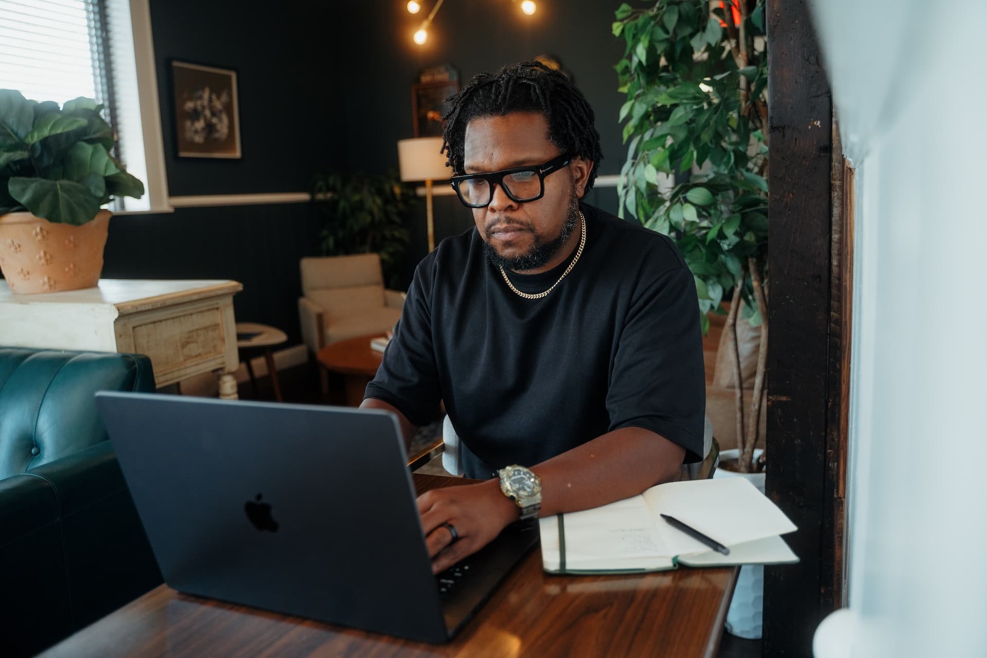 Will Lucas working at a wooden desk on a MacBook in a warm, plant-filled interior.